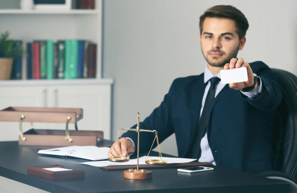 Un jeune avocat en costume assis à son bureau présente sa carte de visite professionnelle.