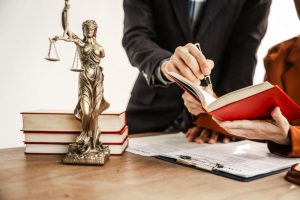 Un avocat conseille une cliente en pointant un document dans un livre de droit à côté d'une statue de la Justice
