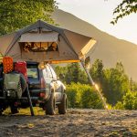man in green jacket sitting on black and yellow camping chair near tent during daytime
