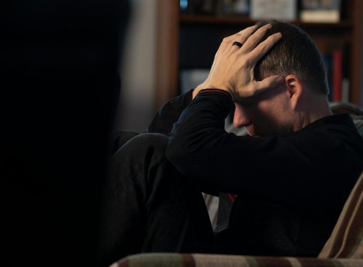 a man sitting on a couch holding his head in his hands